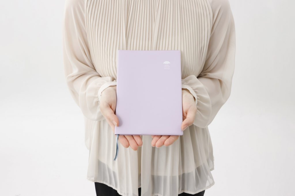 10thly Journalを両手で抱えるように持つ様子
